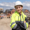 Portrait of young woman construction worker in safety gear standing confidently on building site