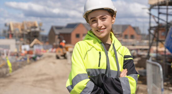 Portrait of young woman construction worker in safety gear standing confidently on building site